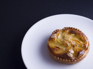 Almond and pear tart on white plate and black background