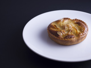 Almond and pear tart on white plate and black background
