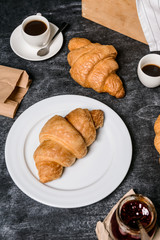 Picture of croissants, pot with jam and coffee cup aside on grey table