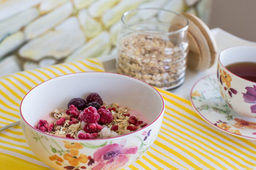 healthy breakfast with natural yogurt, muesli and berries in plate in flower on white tray