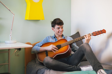 Teenage boy playing guitar in his room © cherryandbees