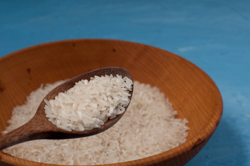 Raw rice in wooden bowl with wooden spoon on blue background