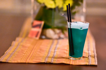 A green cocktail on a table in a bar. It is decorated with fruit ( raspberry). Blurred background of a flowerpot