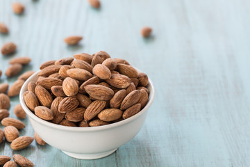 Almonds In White Bowl and Scattered on Blue Wood Background