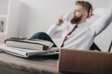 documents and folders on table in office with businessman on background, selective focus