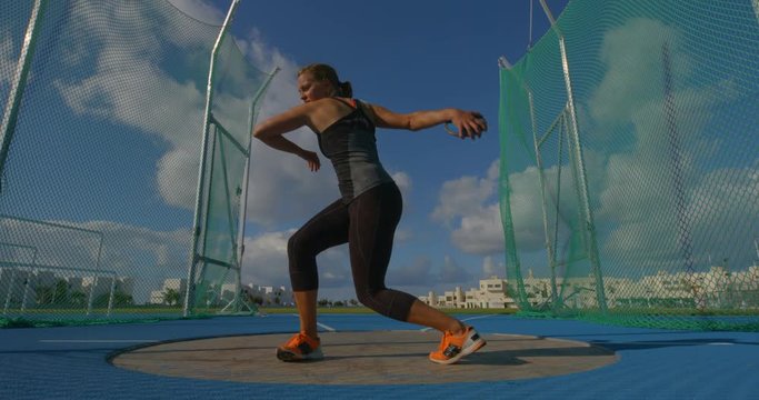 A young woman throwing the discus in the nets.