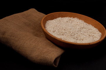 Closeup rice in wooden bowl with wooden spoon on black background empty space
