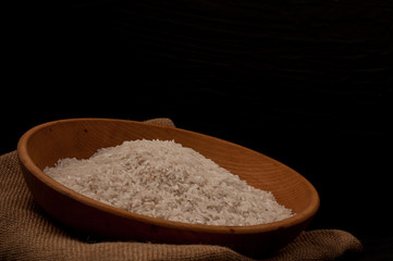 Fototapeta na wymiar Closeup rice in wooden bowl with wooden spoon on black background empty space