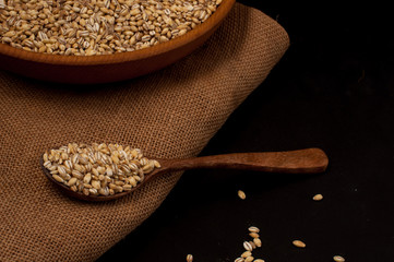 Whole grain of pearl barley or wheat spill on right black background. Agriculture food raw seed.
