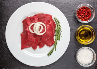 Meat, beef, on a plate. Onion, rosemary, butter, pepper. Still in the background of natural stone, slate