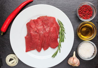 Meat, beef, pepper, garlic, onion, rosemary, red pepper, olive oil, salt. On a white plate, on a board of dark natural stone