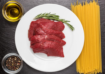 Raw beef meat with rosemary, olive oil, pepper and raw pasta on a stone background