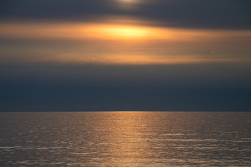 Sunset over horizon on tranquil water surface. Golden sunlight reflecting in water at the beach in late evening.