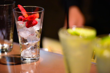 A large glass with ice, raspberries and sliced ​​strawberries. Two other cocktails blurred in the foreground
