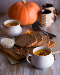 Roasted pumpkin and carrot soup with cream and pumpkin seeds on white wooden background. Copy space