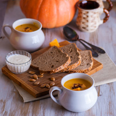 Roasted pumpkin and carrot soup with cream and pumpkin seeds on white wooden background. Copy space