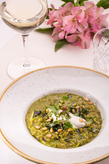 Table layout. Orzotto with goat cheese and spinach. Giving on a round plate with a glass of white wine and fresh flowers