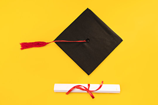 Top view of graduation mortarboard and diploma on yellow background, education concept
