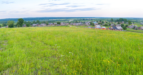 Panorama of village with wooden houses and green meadow in foreground. Arkhangelsky region, Russia. 
