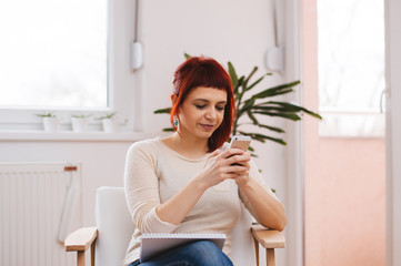 Happy red haired girl is sitting and texting via phone