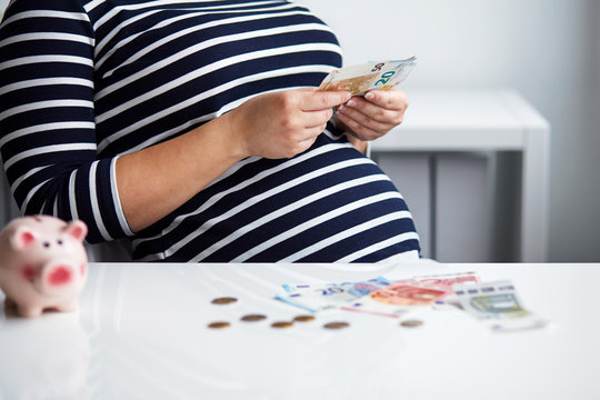 Pregnant woman behind the desk in the office counting money