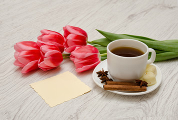 Obraz na płótnie Canvas Coffee mug with spices, clean note, pink tulips on a wooden background, spring breakfast