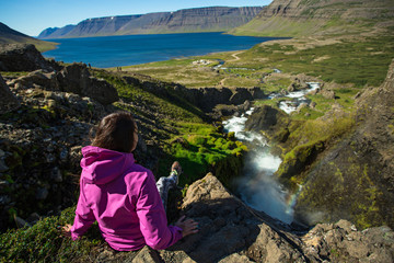 Naklejka premium Girl sitting on the edge of a mountain. Dynjandi waterfall, Iceland.