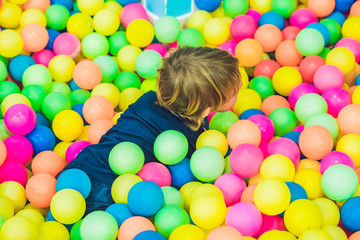 Fototapeta na wymiar Happy little kid boy playing at colorful plastic balls playground high view. Funny child having fun indoors