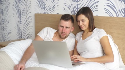 Young couple with laptop watching movie in bed
