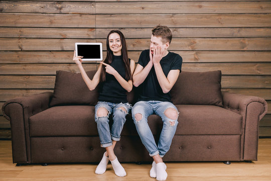 man and woman sitting on sofa with white tablet