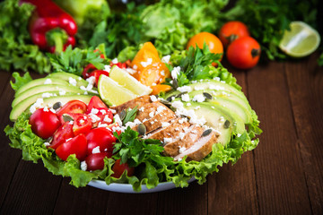 Healthy salad plate with colorful tomatoes, chicken, cheese, avocado, lime and mixed greens on wooden background close up. Food and health. Nutritious meal.