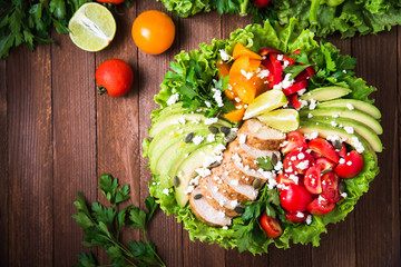 Healthy salad plate with colorful tomatoes, chicken, cheese, avocado, lime and mixed greens on wooden background top view. Food and health. Nutritious meal.
