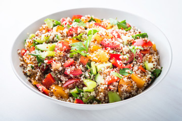 Fresh healthy salad with quinoa, colorful tomatoes, sweet pepper, cucumber and parsley on white wooden background close up. Food and health. Superfood.
