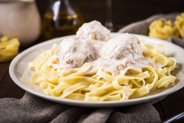 Pasta tagliatelle plate with meatballs and creamy sauce on dark wooden background close up. Italian cuisine. Delicious meal.