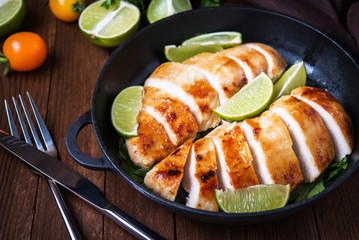 Sliced grilled chicken breasts with lime and parsley on dark wooden background close up. Healthy food.