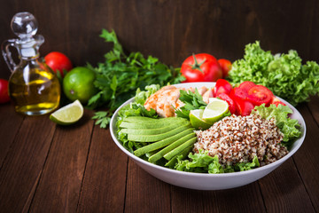 Healthy salad bowl with quinoa, tomatoes, chicken, avocado, lime and mixed greens (lettuce, parsley) on wooden background close up. Food and health.