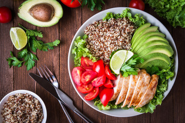 Bol à salade sain avec quinoa, tomates, poulet, avocat, citron vert et mesclun (laitue, persil) sur fond de bois vue de dessus. Nourriture et santé.