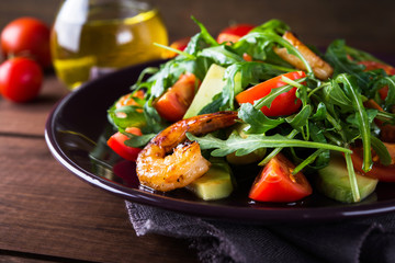 Fresh salad plate with shrimp, tomato, avocado and arugula (salad rocket) on wooden background close up. Healthy food. Clean eating.