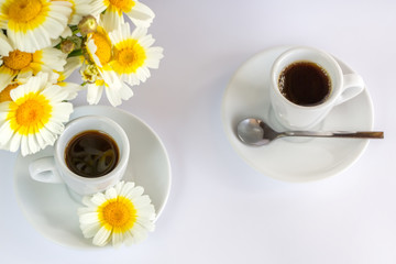 Two cups of coffee and a bouquet of camomiles on a white background
