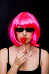 Fototapeta premium Beauty Woman With Pink Wig And Sunglasses and holding with her hand a candy with heart shape