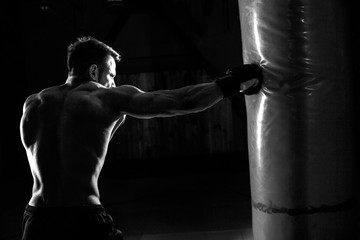 Fototapeta na wymiar Young male boxer hitting punching bag on black background.