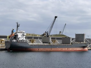 Harbour crane discharging cargo on a general cargo ship in the port of Saint-Malo, Brittany, France. Stern view with cargo hatches open. © targa56
