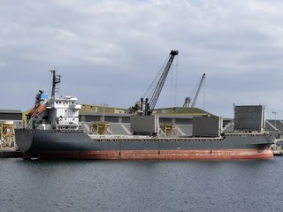 Harbour crane discharging cargo on a general cargo ship in the port of Saint-Malo, Brittany, France. Stern view with cargo hatches open.