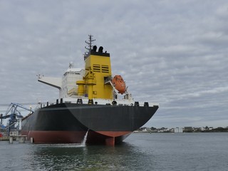 Fototapeta premium Products Tanker discharging at the Oil Terminal of Lorient, France, with black hull and yellow funnel on a cloudy day. Horizontal stern view