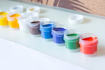 gouache. 8 gouache jars in a row. colorful gouache paint containers.rainbow gouache and piece of white paper