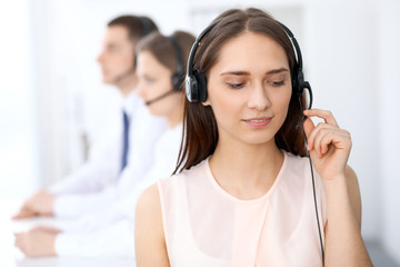 Call center operators. Focus at young beautiful business woman in headset.