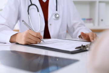 Fototapeta premium Close up of a female doctor filling up an application form while consulting patient. Medicine and health care concept