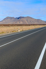 Road in desert landscape and volcanic mountains in background, Fuerteventura, Canary Islands, Spain