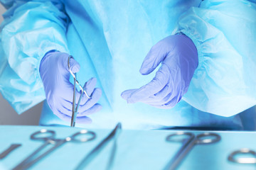 Close-up of of surgeons hands at work in operating theater toned in blue. Medical team performing operation