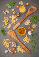 Italian foods concept and menu design.Various kind of pasta with ingredients sweet basil ,tomato ,garlic ,parsley ,champignon and extra virgin olive oil on dark stone background flat lay.